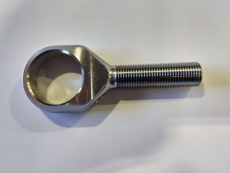 A stainless steel nut during manufacturing on a white surface.