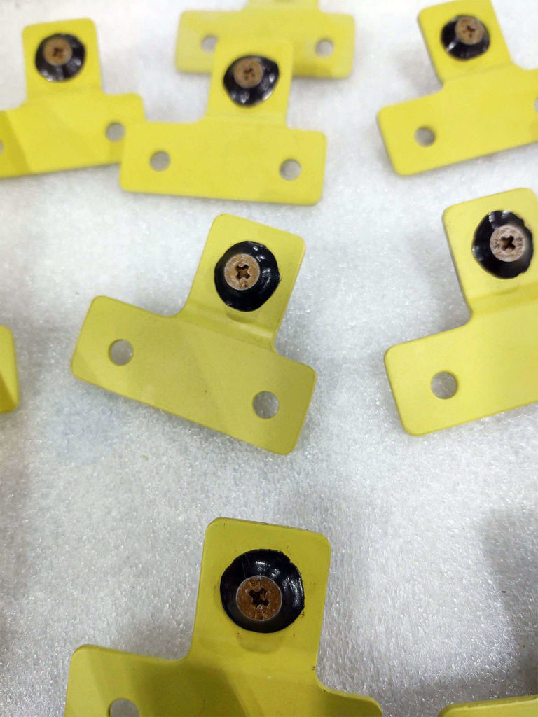 A group of yellow plastic brackets undergoing assembly on a white surface.